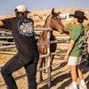 Two people with a grey and green 'OFFSEASON' t-shirt interacting with a horse behind a fence in an outdoor setting