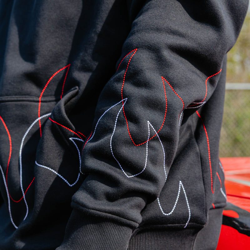 Close-up of layered red and white stitched flame outlines across the sleeve of a black hoodie