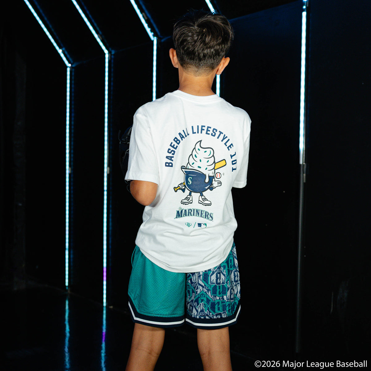 Youth model wearing green youth shorts with "Seattle Mariners Sticker Court" design