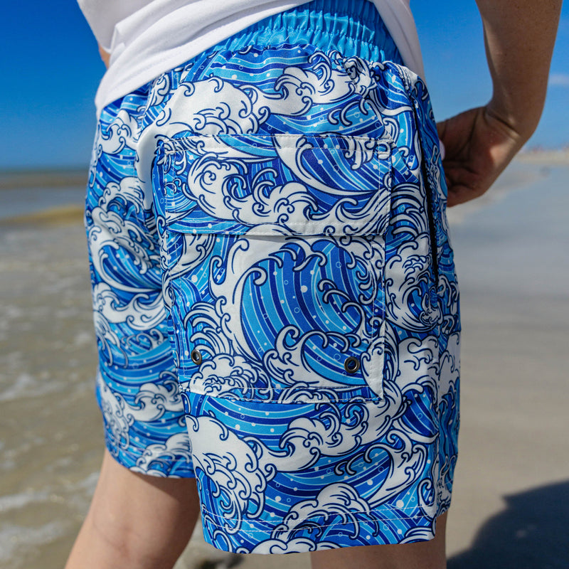 Back side view of BL101 wave print swim trunks at the beach, highlighting the cargo pocket detail and all-over wave pattern.